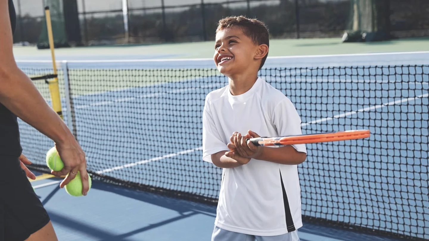 A young tennis player smiling beside a coach on court