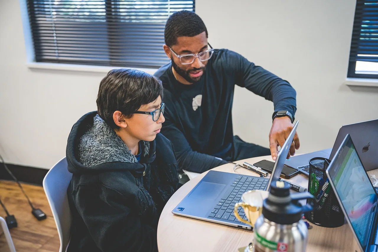 An adult guiding a student through work on a laptop
